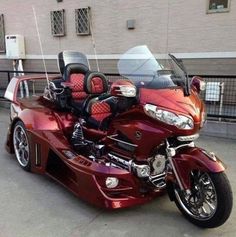 a red motorcycle parked on the street next to a car with two seats in it