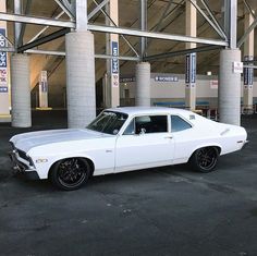 a white muscle car parked in a parking lot next to some tall pillars with signs on them