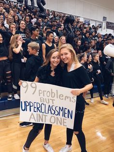 two young women holding a sign in front of a large group of people on a basketball court