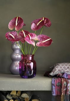 a purple vase filled with pink flowers sitting on top of a shelf next to logs