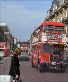 a red double decker bus driving down a street next to tall buildings and people walking on the sidewalk