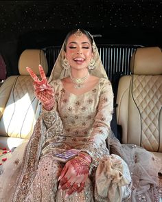 a woman sitting in the back of a car wearing a bridal gown and holding her hand up