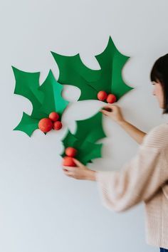 a woman is holding up some paper holly decorations