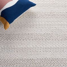 a white rug with blue, pink and yellow pillows on it's sides next to a pillow