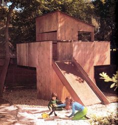 two children playing in the sand near a wooden structure with a slide and climbing wall