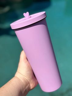 a person holding a pink cup with a lid in front of a blue swimming pool