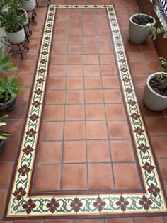 a tiled walkway with potted plants on the side and an ornamental border around it