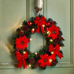 a christmas wreath with red poinsettis and pine cones hanging on a door