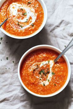 two bowls of tomato soup with parmesan cheese on the top and fresh herbs in the middle