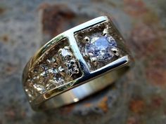 a ring with three diamonds on it sitting on top of a stone slab in front of a rock