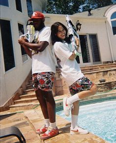 two people standing next to each other in front of a pool holding tennis racquets