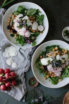 two white bowls filled with salad next to radishes and other vegetables on a table