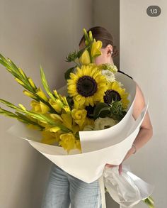 a woman holding a bouquet of sunflowers in front of her face and looking at the wall