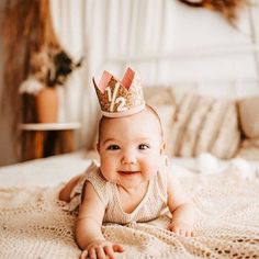 a baby laying on top of a bed wearing a crown