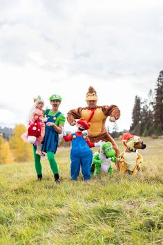 three people in costumes are standing on the grass with stuffed animals and one person is holding a toy