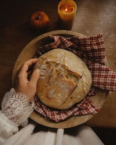 a person holding a piece of bread on top of a wooden plate next to a candle