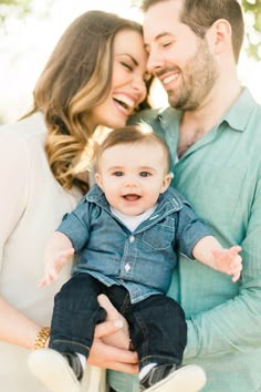 a man and woman smile as they hold their baby boy in front of the camera