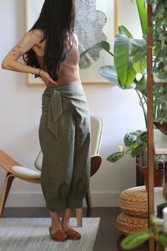 a woman standing in front of a plant with her back to the camera, wearing green pants