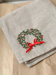 two napkins with red ribbon and holly wreath on them sitting on top of each other