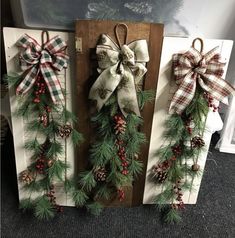 three christmas wreaths with bows and pine cones hanging on the wall in front of a fireplace