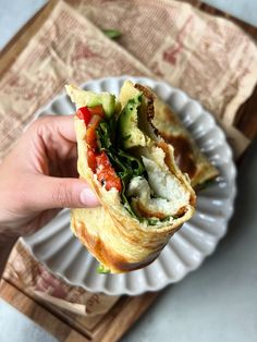 a person is holding up a sandwich on a plate with other food items in the background