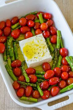 a casserole dish with tomatoes, asparagus and feta cheese in it