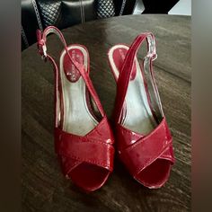 Red Slingback Heels With A Glossy Finish. They Have An Open Toe Design And Feature A Cork-Patterned Platform And Heel. The Strap Around The Back Has A Buckle For Adjustment, Adding Both Style And Support. These Shoes Combine Elegance With A Touch Of Casual Flair, Making Them Versatile For Various Occasions. Red Slingback Sandals With 4-inch Heel, Red Synthetic Slingback Sandals With Round Toe, Red Synthetic Round Toe Slingback Sandals, Red Synthetic Slingback Sandals With Heel Strap, Red Synthetic Slingback Pumps, Red Synthetic Slingback Heels, Red Slingback Heels With 4-inch Heel, Red 4-inch Heel Slingback Heels, Red Open Toe Slingback Pumps