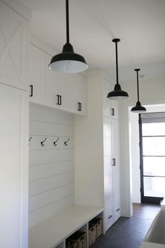 a kitchen with white cabinets and hanging lights over the counter top, along with two black pendant lights