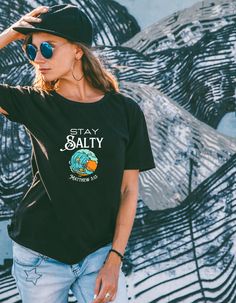 Unleash your inner surfer with this eco-friendly t-shirt that showcases a skeleton shredding a wave and clutching a cross. Plus, for a biblical twist, we tucked in Matthew 5:13 at the bottom of the wave. This one-of-a-kind design was a custom ask and it came out just right! Our Re-Tee is crafted from 100% recycled fabric, never dyed again, using rescued materials that would have wound up in the junkyard. Soft. Cozy. Top-notch. When you're doing good for Mother Earth, it's a good feeling for your Black Surfing T-shirt With Screen Print, Casual Black T-shirt For Surfing, Black Graphic Tee For Surfing, Black Screen Print Surfing T-shirt, Black Graphic Print T-shirt For Surfing, Black Surfing T-shirt With Letter Print, Black Letter Print T-shirt For Surfing, Surfing Skeleton, Matthew 5 13