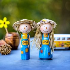 two wooden dolls standing next to each other on a blue table with pine cones and flowers in the background