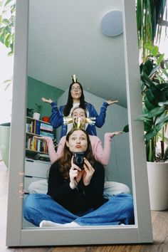 three women sitting on the floor in front of a mirror taking a selfie with their cell phone