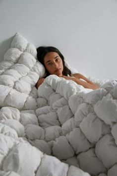 a woman is laying in a bed with white sheets