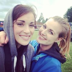 two young women standing next to each other in front of a soccer field with grass