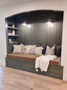 a bench with pillows and blankets on it in a room that has wood paneling