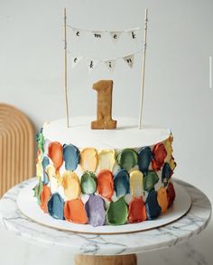 a multicolored cake with the number one on top is sitting on a table