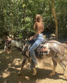 a woman riding on the back of a brown and white horse next to a forest