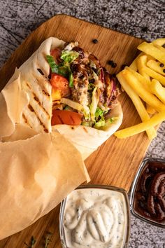 a pita sandwich with fries and ketchup on a cutting board next to dipping sauce