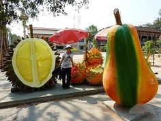 there is a giant pumpkin and other fruit on the side of the road with people standing next to it