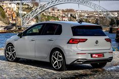 the rear end of a white volkswagen car parked in front of a bridge and water