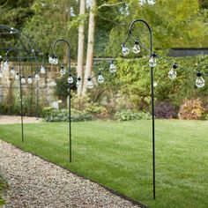 some lights are hanging on poles in the grass near a path and trees with green grass