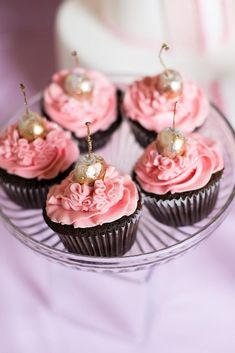 cupcakes with pink frosting and gold decorations on a glass platter, ready to be eaten