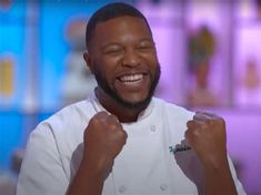 a man in a chef's uniform smiling and holding his fist up to the camera