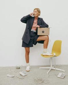 a woman sitting on top of a yellow chair talking on a cell phone and holding a box