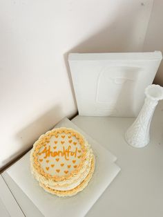 there is a cake on the table next to a white vase and card holder that says thank you