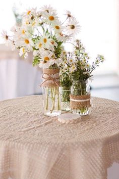 two mason jars with daisies tied to them are sitting on top of a table