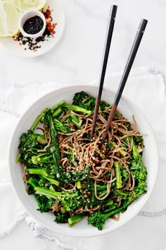 a bowl filled with noodles and broccoli on top of a white table cloth