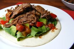 a tortilla topped with meat, lettuce and tomatoes