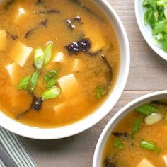 two bowls filled with soup on top of a wooden table next to chopsticks