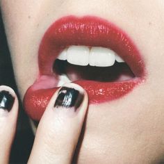 a woman with black and white nail polish holding her finger up to her mouth while wearing red lipstick