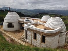 an unusual house built on the side of a hill with mountains in the back ground